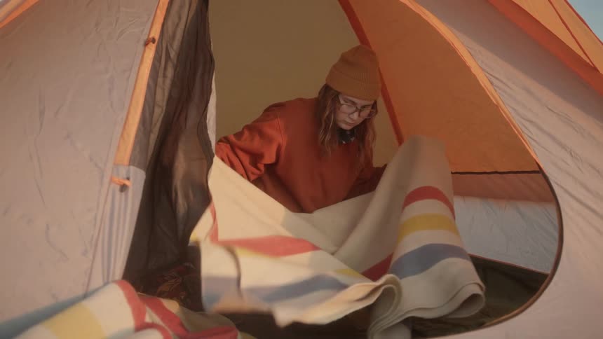A girl unfolds a blanket sitting in a tent