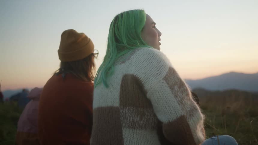 Young female friends sitting outdoors looking at the sunset over the mountains
