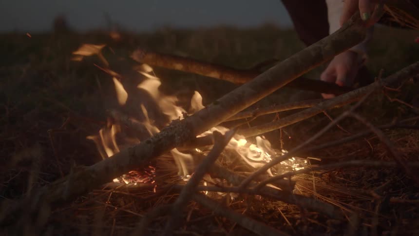 Someone is building a camp fire and putting more sticks on the flames
