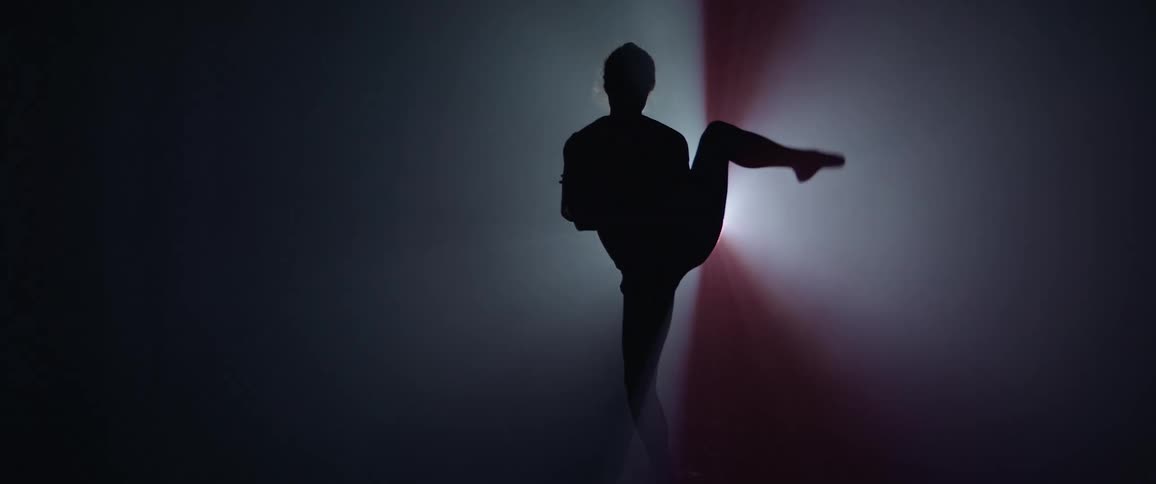 Silhouette of a woman performing dance poses in front of a projector in a dark room
