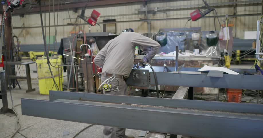 Man uses a mig welder and a hammer while working in a workshop