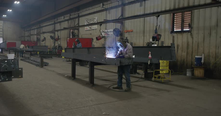 A person with a welding helmet and a torch welding in a factory