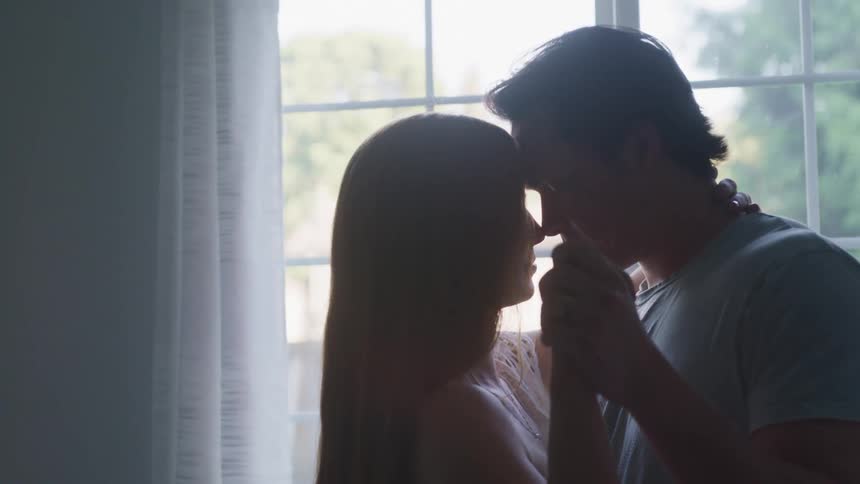 A woman and a man slow dance together in front of a window in a building during the day