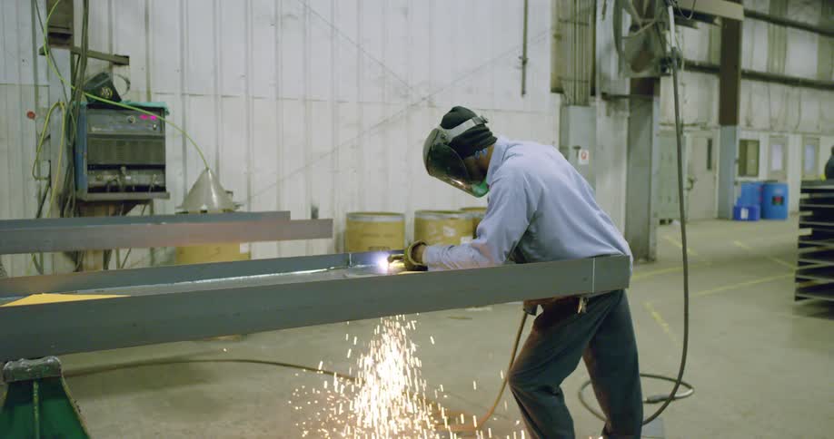 Construction worker welding metal frames in a factory inside a warehouse