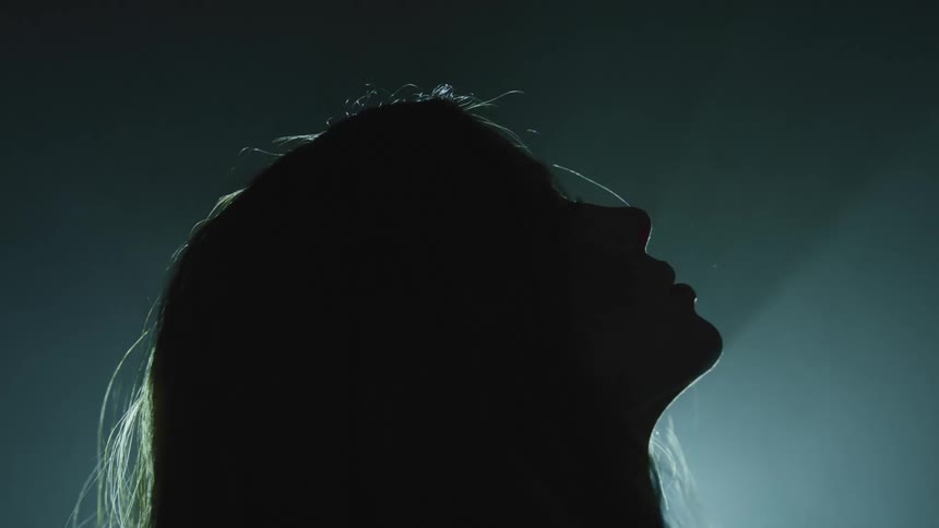 Silhouette of a woman looking upwards as a beam of light flickers behind her