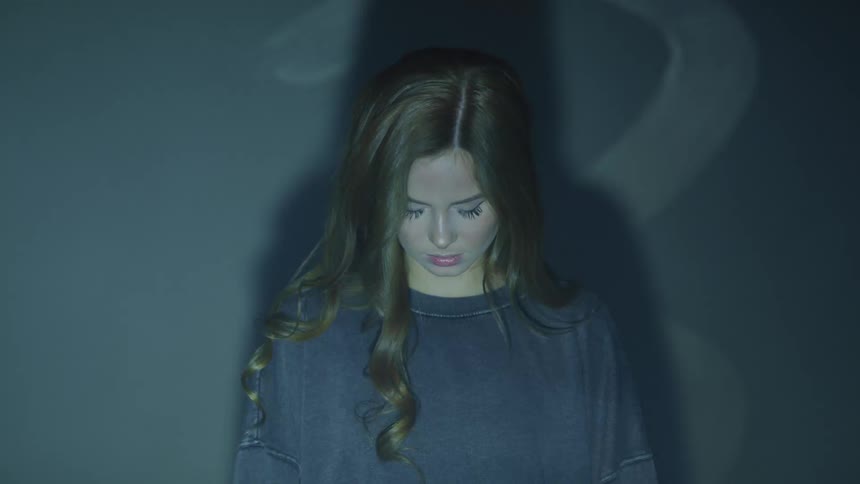 Woman stands against wall casting shadow as symbols are projected over her