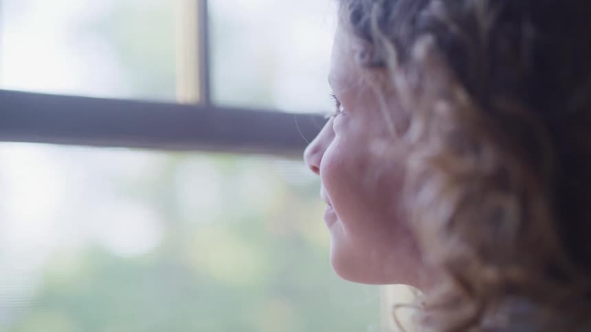 Young girl with curled hair looking happily out the window