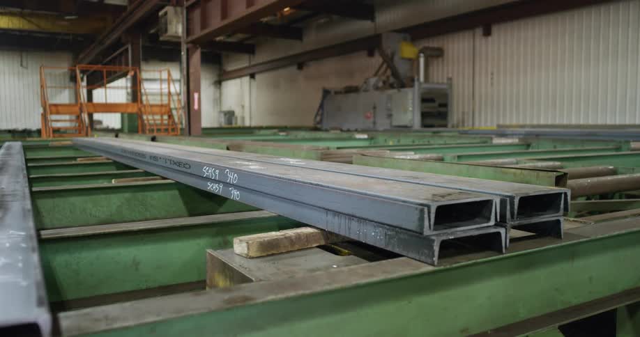 Long metal profiles being placed over a rack using a forklift in a factory inside a warehouse