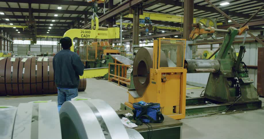Man working a crane on a large machine inside of a warehouse at daytime