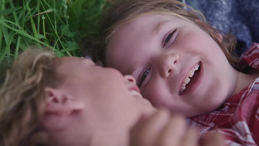 Two white kids laying down in the grass while talking and laughing together