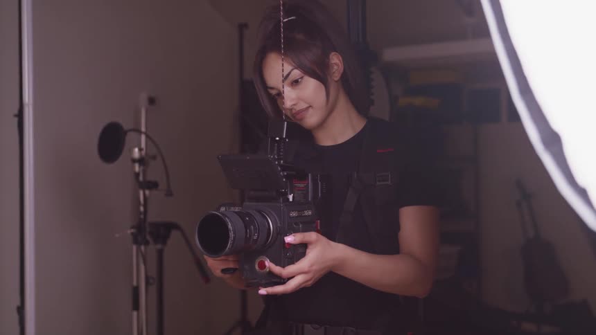 Filmaker filming inside a dimly lit studio next to a lamp with a video camera