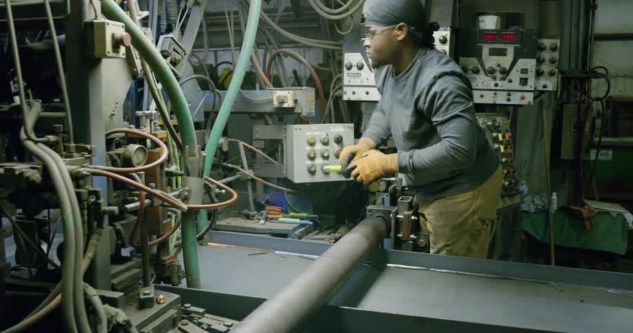 A man in a workshop with goggles using a measuring tape and turning on machinery