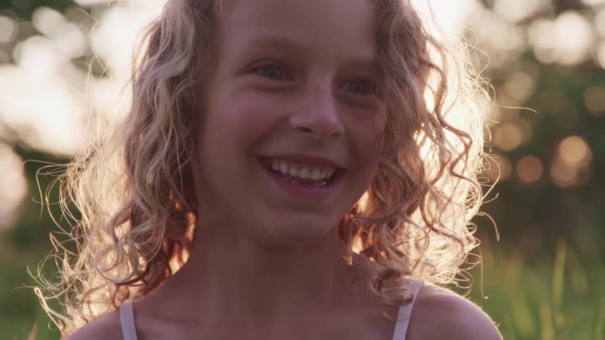 Young blonde girl smiling and looking at the camera in a grass field at sunset