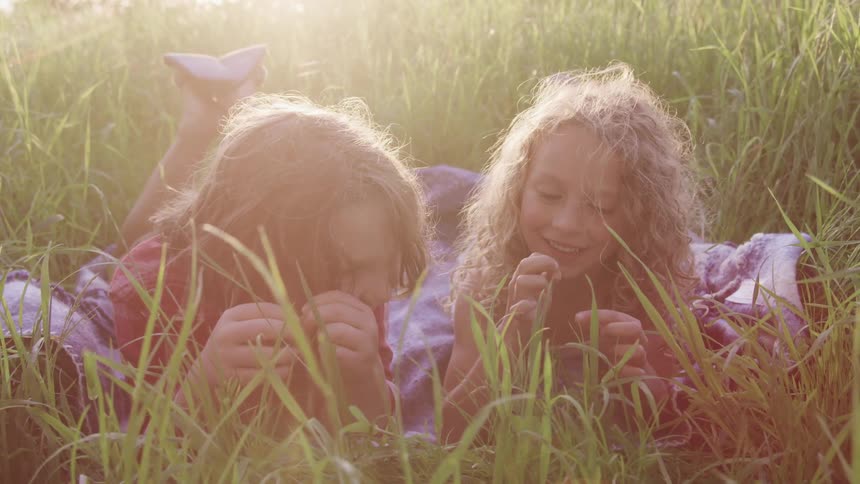 Two girls laying on a grassy field and smiling
