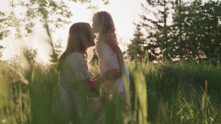 A mother is outdoors sitting in the grass with her daughter at dusk