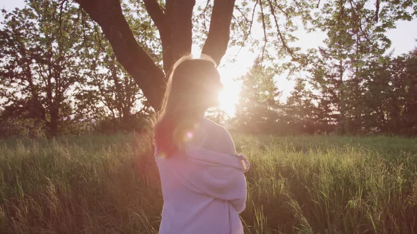 A woman standing in the middle of field surrounded by a forest