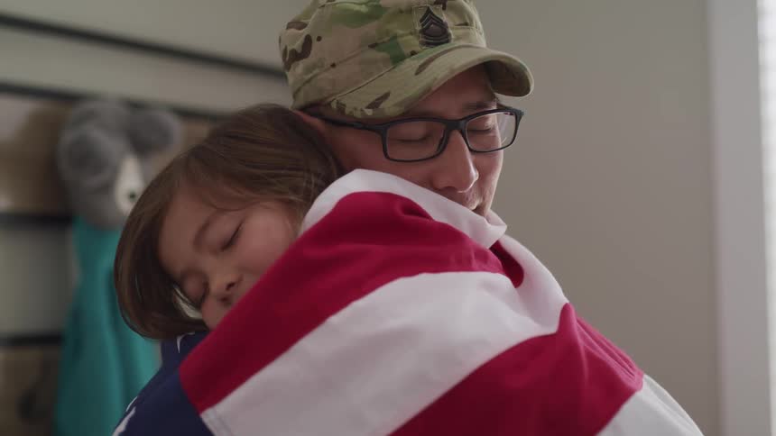 A soldier hugs his daughter who has a flag wrapped around her body