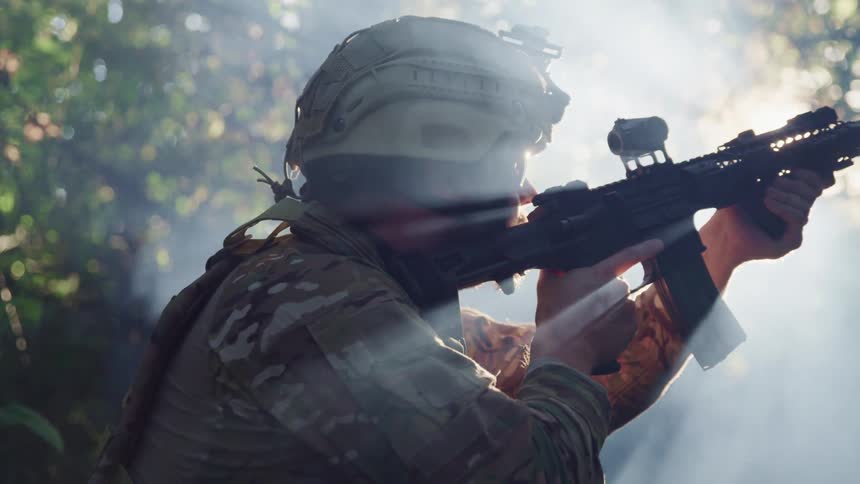Male solider stands aiming down scope with sunlight streaming in through trees