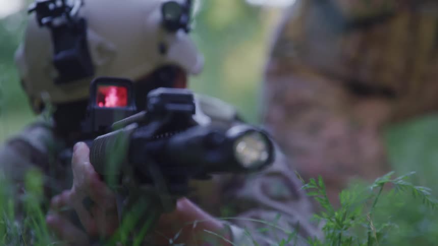 Soldier prone in the ground on a forest pointing an assault rifle