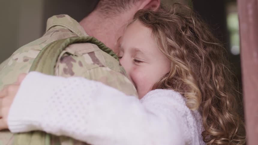 A young girl smiles as she hugs her dad who is in a military uniform