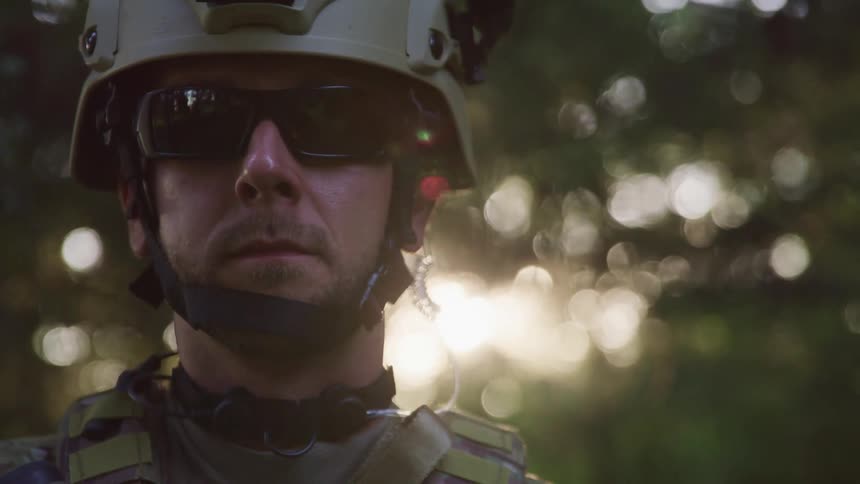 A male soldier stands outdoors in camouflage helmet and sunglasses