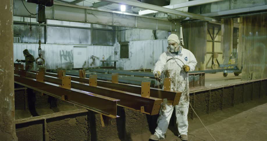 A person with a mask and a suit spraying chemicals on metal with a hose