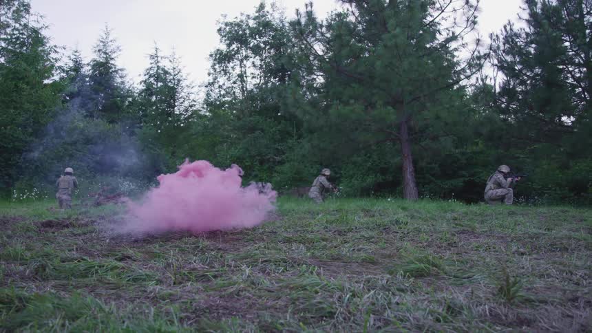 Thick pink smoke rises from the ground behind soldiers situated behind trees with their guns drawn