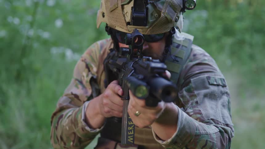 Man wearing combat gear holds firearm panning it around