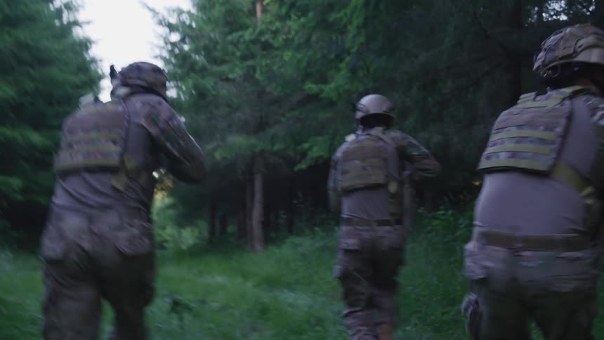 Three military soldiers in camouflage and wearing helmets running in forest with guns