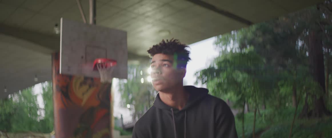 A male teenager shooting hoops outside on a basketball court