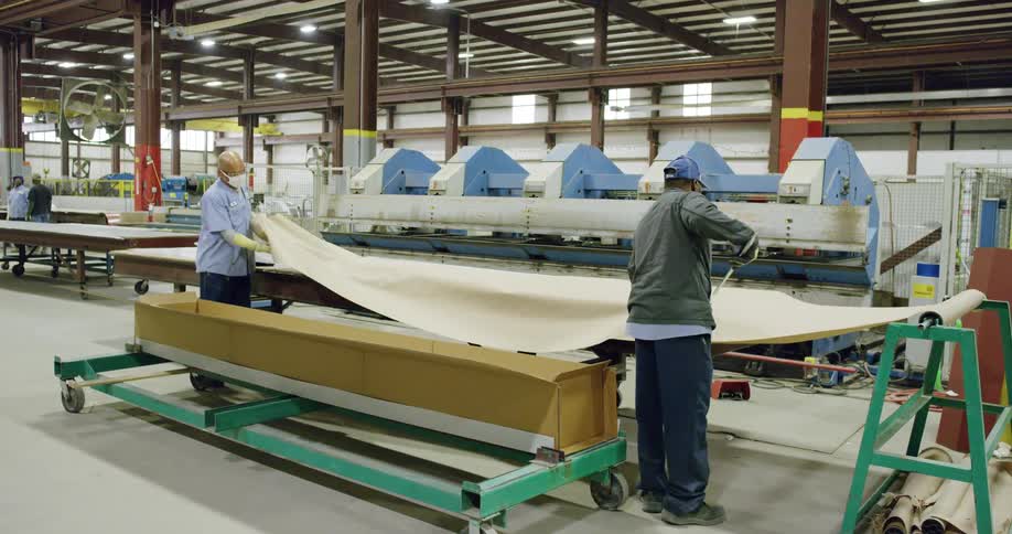 Two workers cutting paper from a roll in a factory inside a warehouse