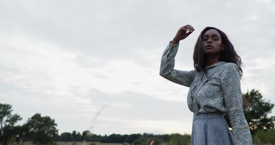 Young long haired woman in a long dress on a grass field at day time