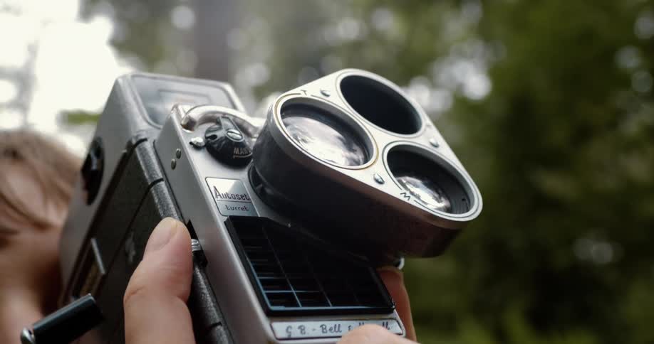 A person films using a vintage camera outside near trees