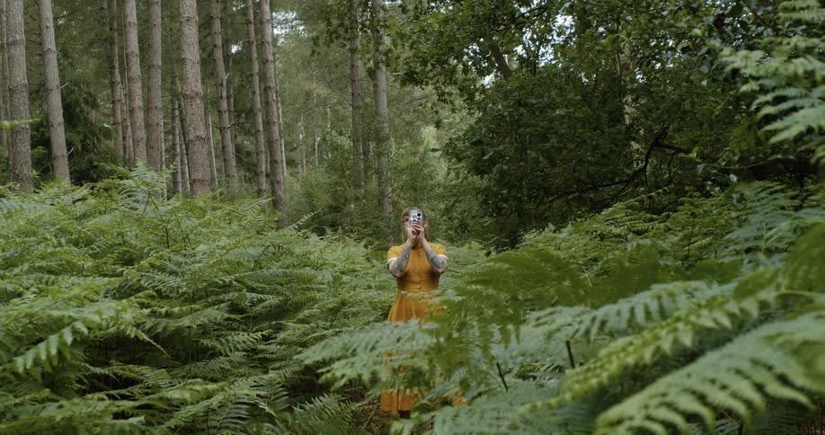 A woman wearing an orange dress films the interior of a forest