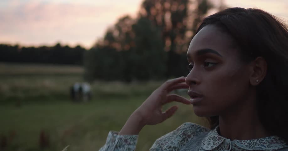 Young woman touching her hair while standing on a field at sunset