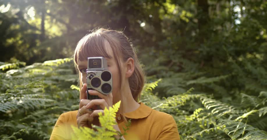 A woman using a retro camera in a high patch of plants