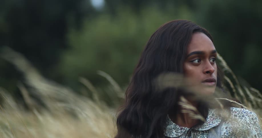 A woman sitting out in a field stares off into the distance