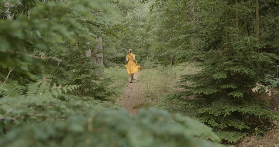 White woman wearing a yellow dress running alone in a trail in the middle of the forest