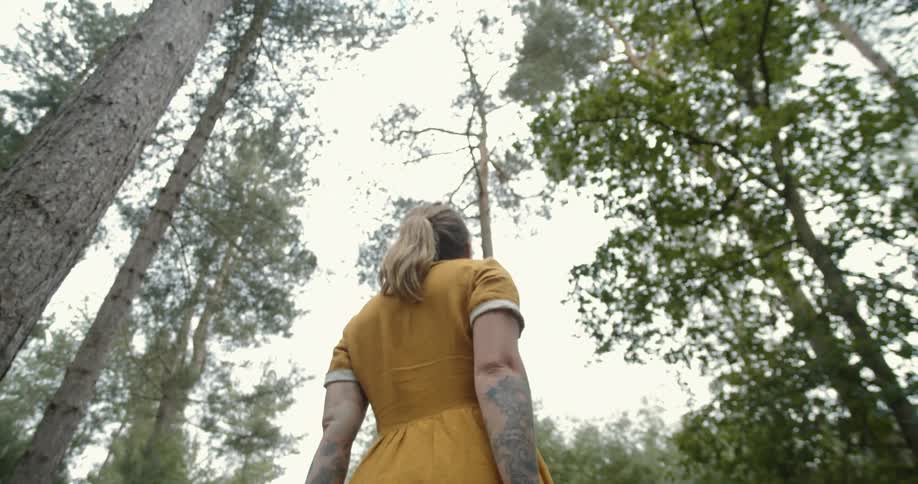 A woman standing in a forest at daytime sways from side to side looking up