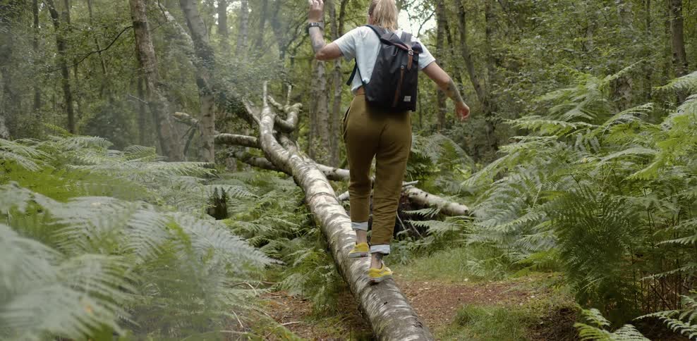 Woman walks and balances across a fallen tree trunk in a forest at daytime