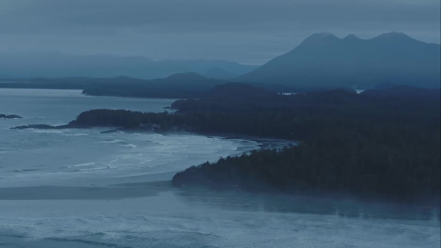 Aerial of Pacific Coastline featuring fog and crashing waves with distant mountains