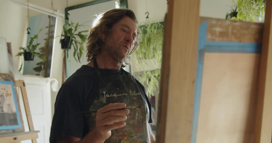 Man painting indoors on a canvas on an easel with paintbrush