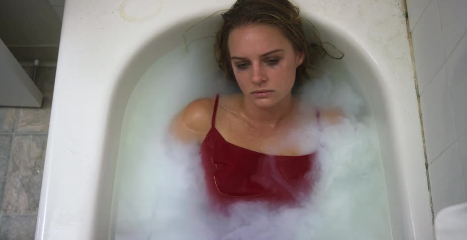 Depressed sad young woman in a red dress laying in a bathtub