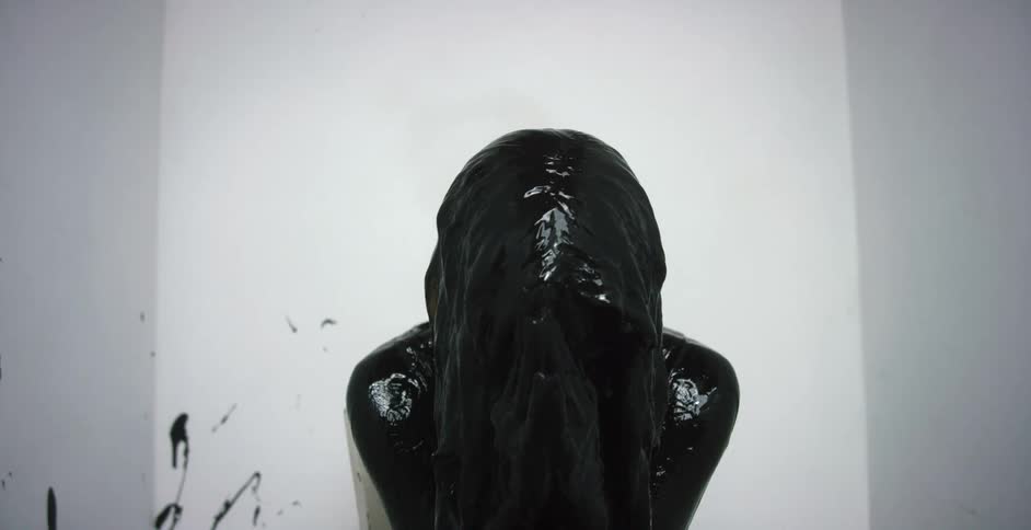 A person sits in a chair covered in black paint rocking back and forth in front of a white paint