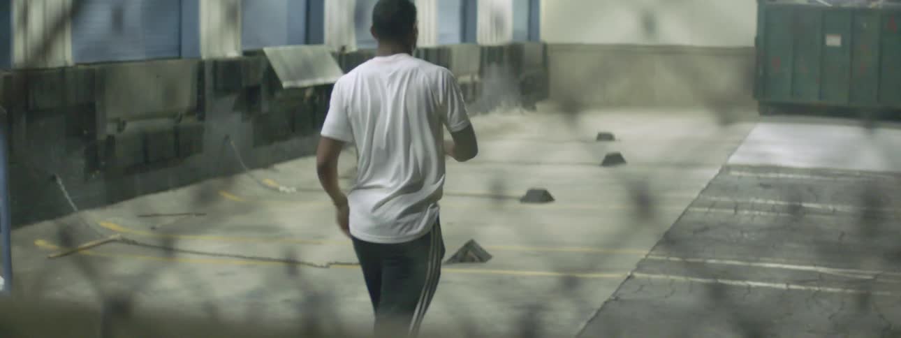 A boy walks past building steps into a parking lot stretching his shoulders and legs