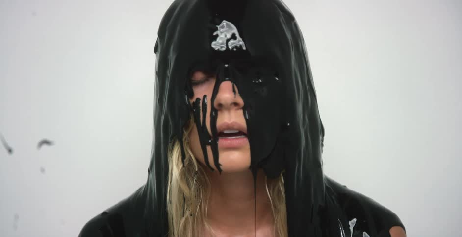 Black paint pours over a womans head who is sitting down inside of a white room