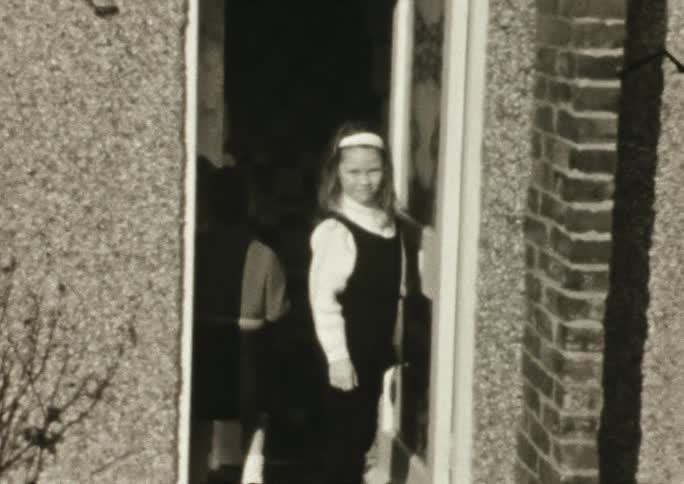A girl standing in the doorway of a house while a boy walks by her into the house to talk to another boy