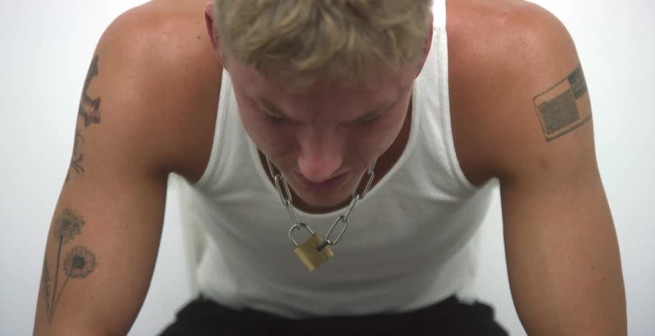 Sad young blonde tatooed man sitting in a corner of a white room crying