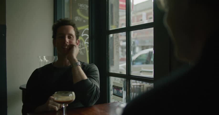 Two men talking to each other at the bar while laughing and drinking cocktails