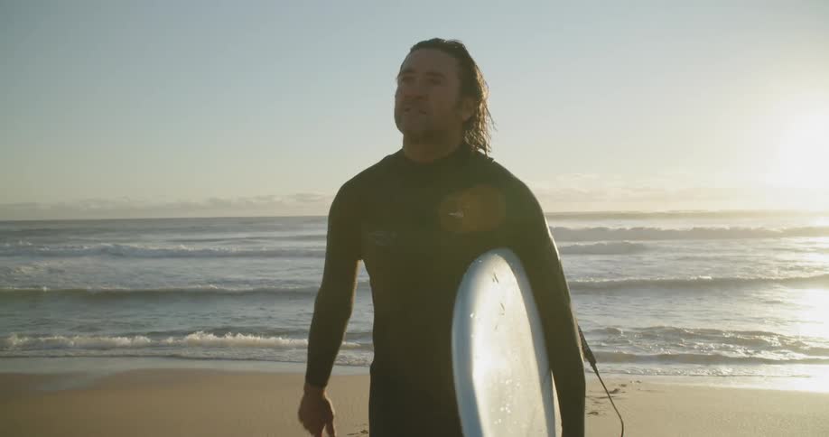 Man holding his surfboard while walking out of the sea